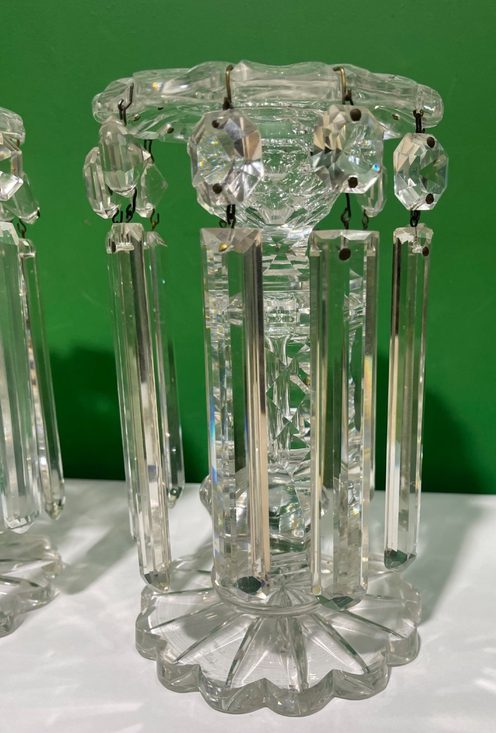 A pair of clear cut glass table lustres featuring faceted stems, starburst cut bases, and hanging crystal prism drops suspended from wire hooks. View VI