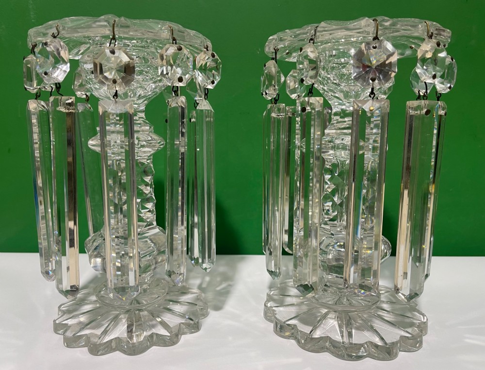 A pair of clear cut glass table lustres featuring faceted stems, starburst cut bases, and hanging crystal prism drops suspended from wire hooks. View X