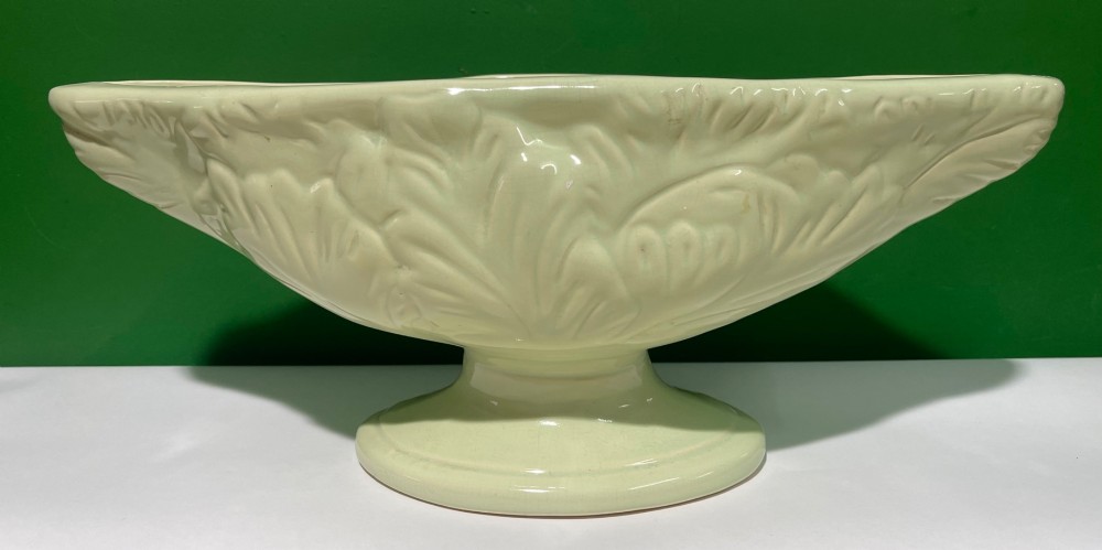 A pale cream glazed ceramic boat-shaped vase featuring embossed lotus leaf reliefs raised on a circular pedestal foot.