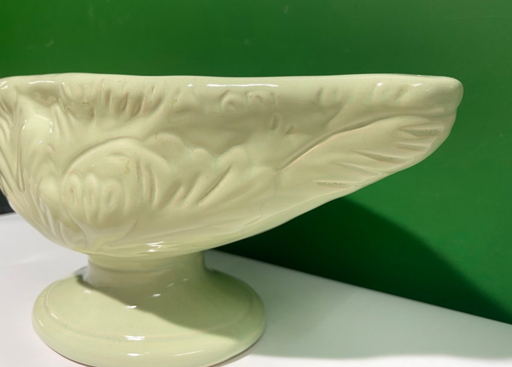 A pale cream glazed ceramic boat-shaped vase featuring embossed lotus leaf reliefs raised on a circular pedestal foot. View III