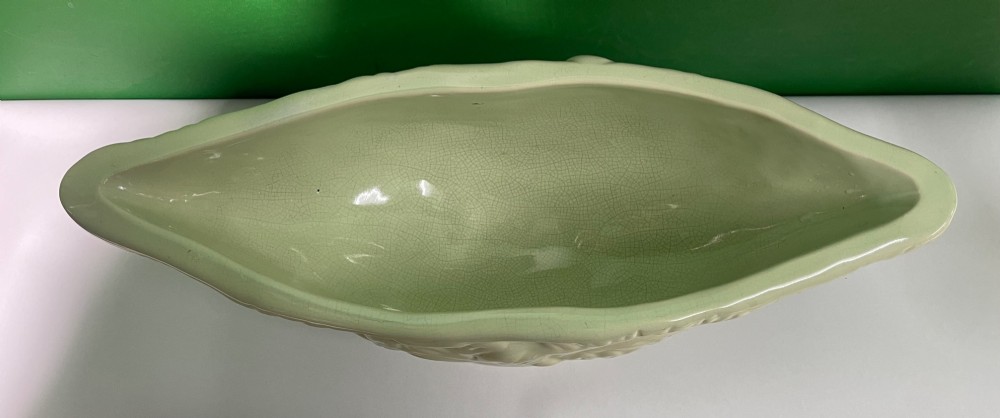 A pale cream glazed ceramic boat-shaped vase featuring embossed lotus leaf reliefs raised on a circular pedestal foot. View IV