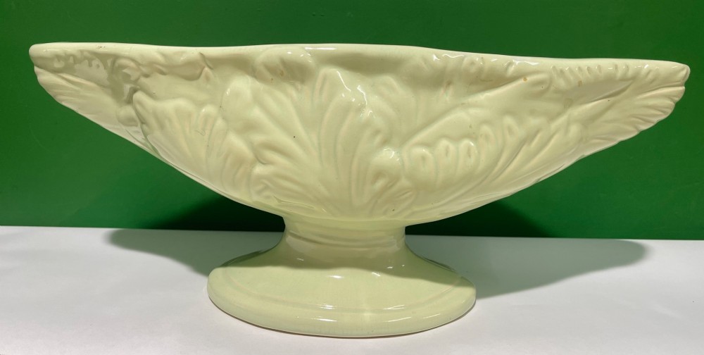 A pale cream glazed ceramic boat-shaped vase featuring embossed lotus leaf reliefs raised on a circular pedestal foot. View V