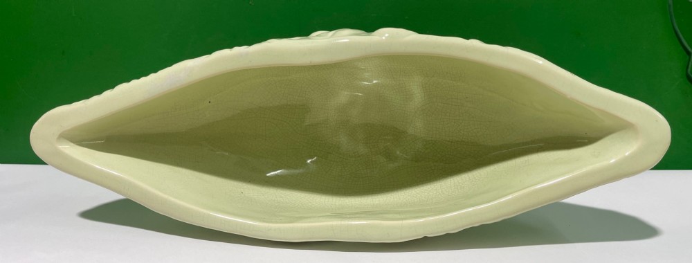 A pale cream glazed ceramic boat-shaped vase featuring embossed lotus leaf reliefs raised on a circular pedestal foot. View VI