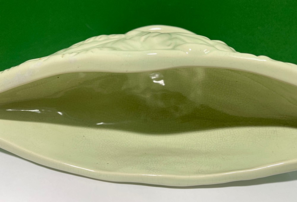 A pale cream glazed ceramic boat-shaped vase featuring embossed lotus leaf reliefs raised on a circular pedestal foot. View VII