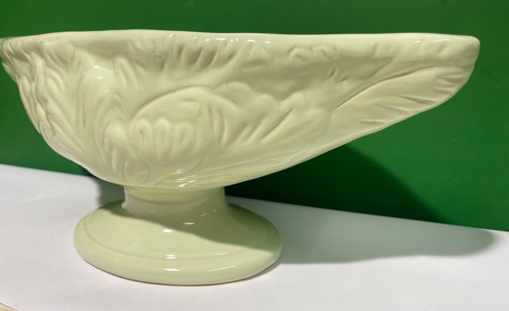 A pale cream glazed ceramic boat-shaped vase featuring embossed lotus leaf reliefs raised on a circular pedestal foot. View VIII