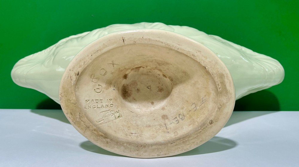 A pale cream glazed ceramic boat-shaped vase featuring embossed lotus leaf reliefs raised on a circular pedestal foot. View IX