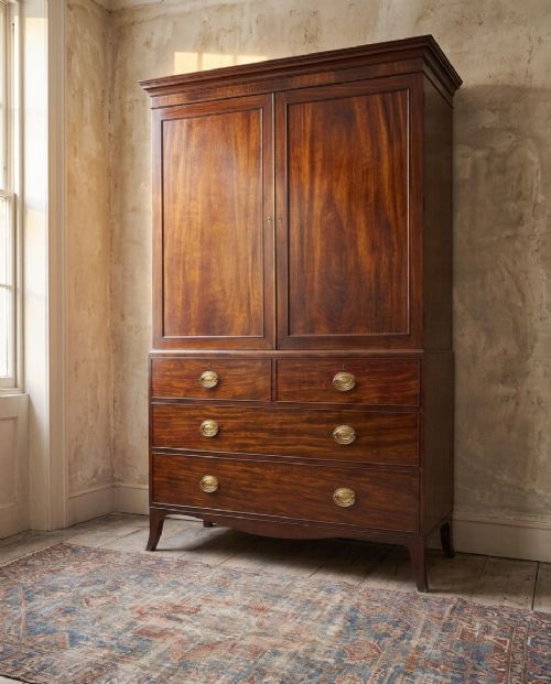 A Regency mahogany linen press featuring an upper two-door cupboard with flame veneer panels above a base of two short and two long drawers with brass handles. View XIII