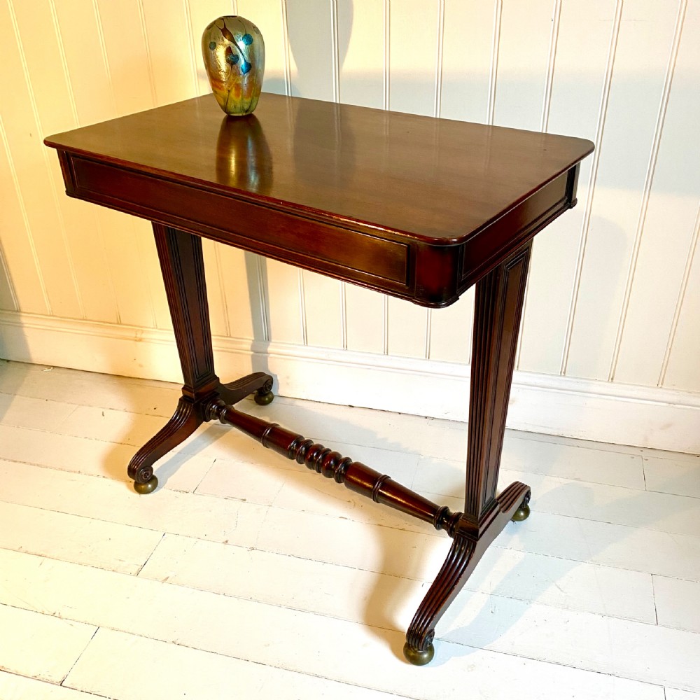 A 19th-century dark mahogany side table featuring a rectangular top, reeded uprights, a turned cross-stretcher, and splayed legs with brass castors. View X