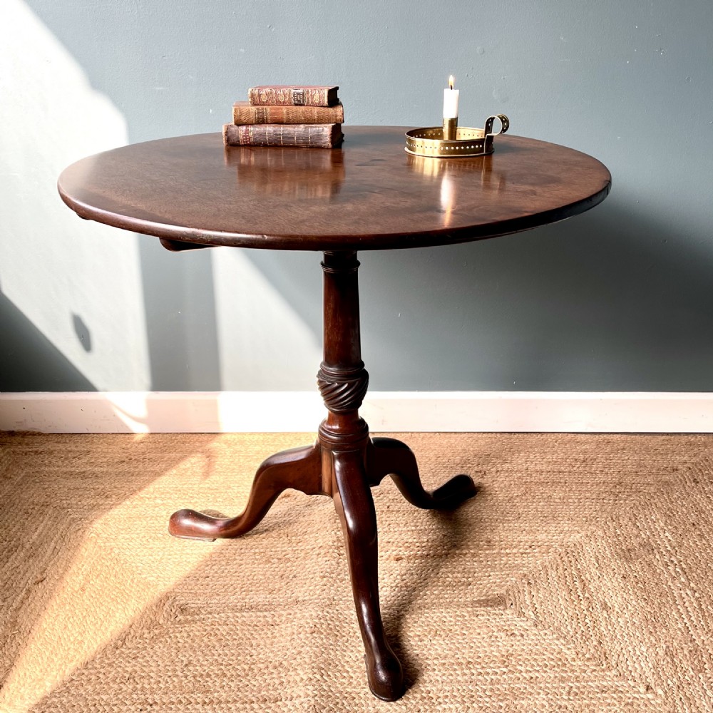 A Georgian mahogany tilt-top tripod table featuring a circular top, turned stem with a spiral carved knop, and three cabriole legs with pad feet.