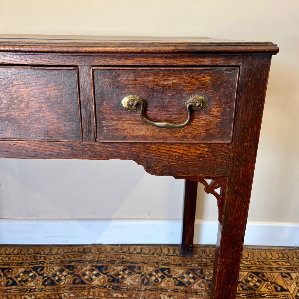 An 18th-century Georgian dark oak lowboy table featuring three drawers with brass swan-neck handles and a shaped frieze. View II