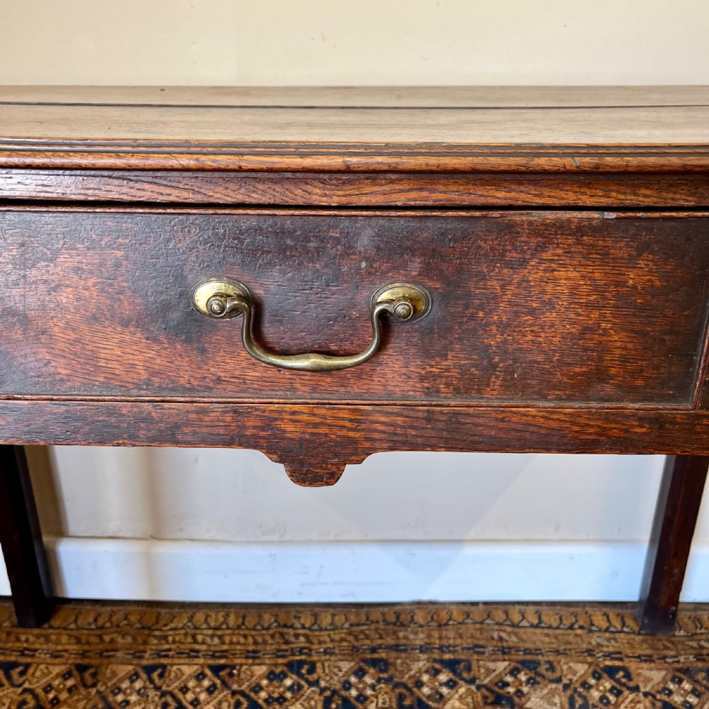 An 18th-century Georgian dark oak lowboy table featuring three drawers with brass swan-neck handles and a shaped frieze. View III