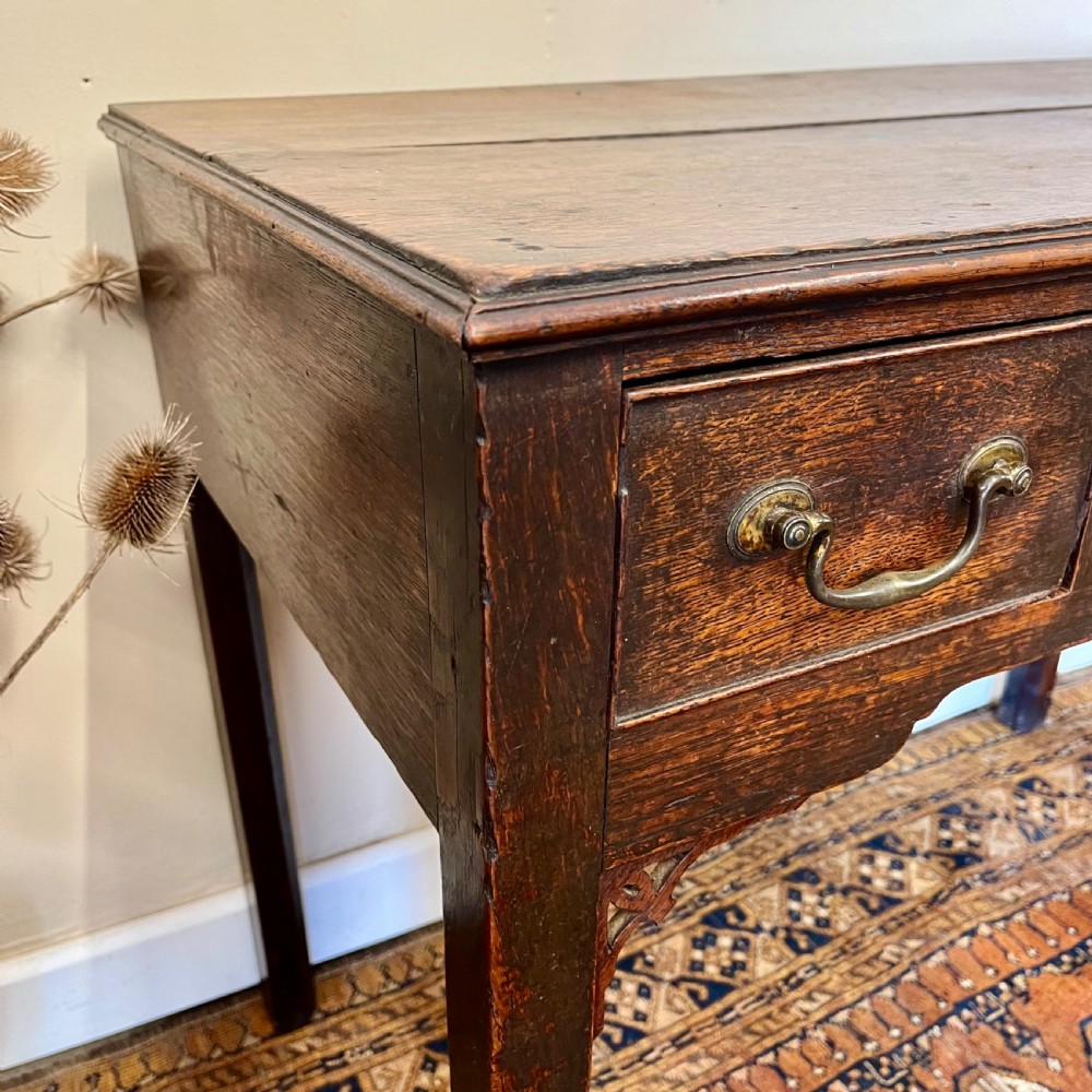An 18th-century Georgian dark oak lowboy table featuring three drawers with brass swan-neck handles and a shaped frieze. View V