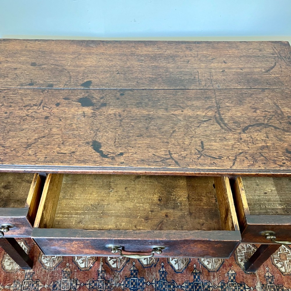 An 18th-century Georgian dark oak lowboy table featuring three drawers with brass swan-neck handles and a shaped frieze. View VI