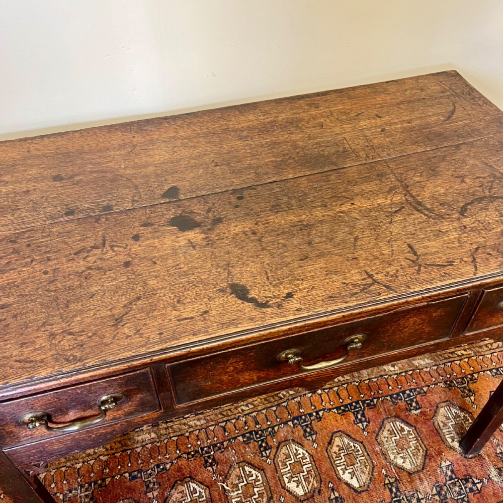 An 18th-century Georgian dark oak lowboy table featuring three drawers with brass swan-neck handles and a shaped frieze. View VII
