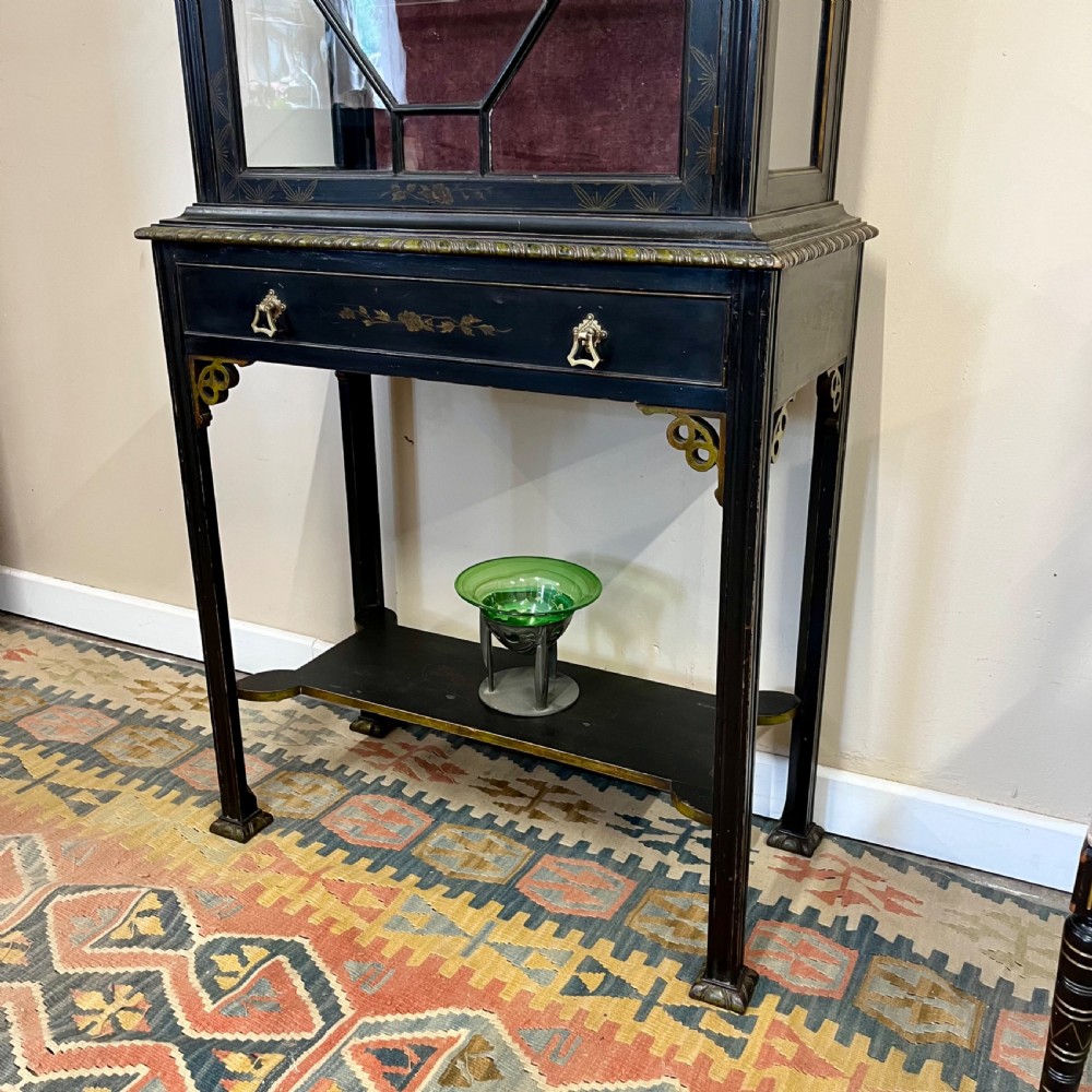An ebonised Aesthetic Movement display cabinet featuring a glazed upper section with geometric glazing bars, hand-painted gilt motifs, a drawer, and slim legs with a bottom tier shelf. View II