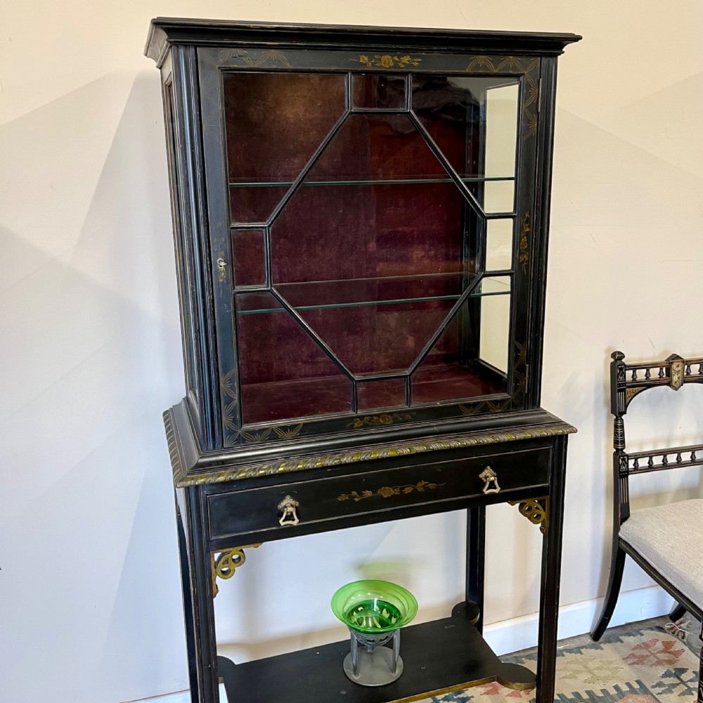 An ebonised Aesthetic Movement display cabinet featuring a glazed upper section with geometric glazing bars, hand-painted gilt motifs, a drawer, and slim legs with a bottom tier shelf. View III
