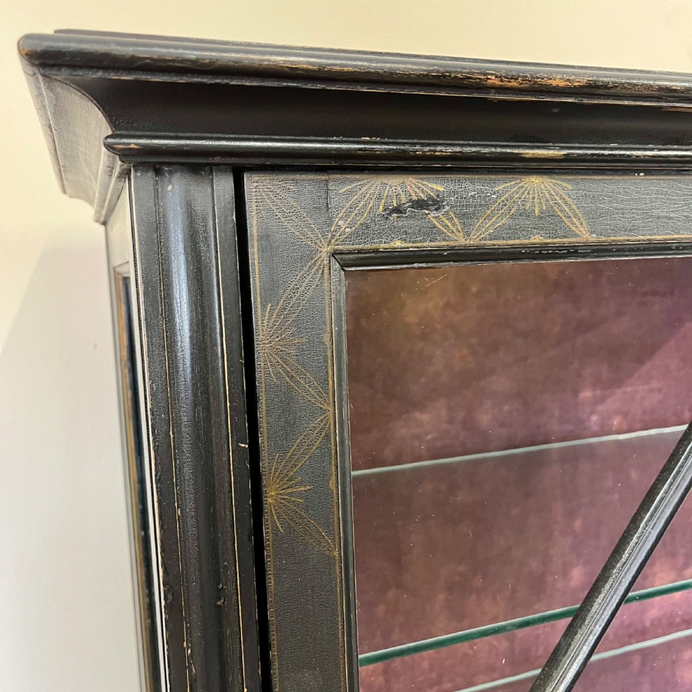 An ebonised Aesthetic Movement display cabinet featuring a glazed upper section with geometric glazing bars, hand-painted gilt motifs, a drawer, and slim legs with a bottom tier shelf. View VIII
