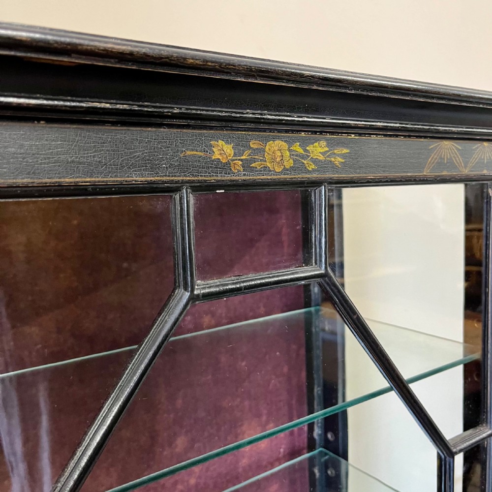 An ebonised Aesthetic Movement display cabinet featuring a glazed upper section with geometric glazing bars, hand-painted gilt motifs, a drawer, and slim legs with a bottom tier shelf. View IX