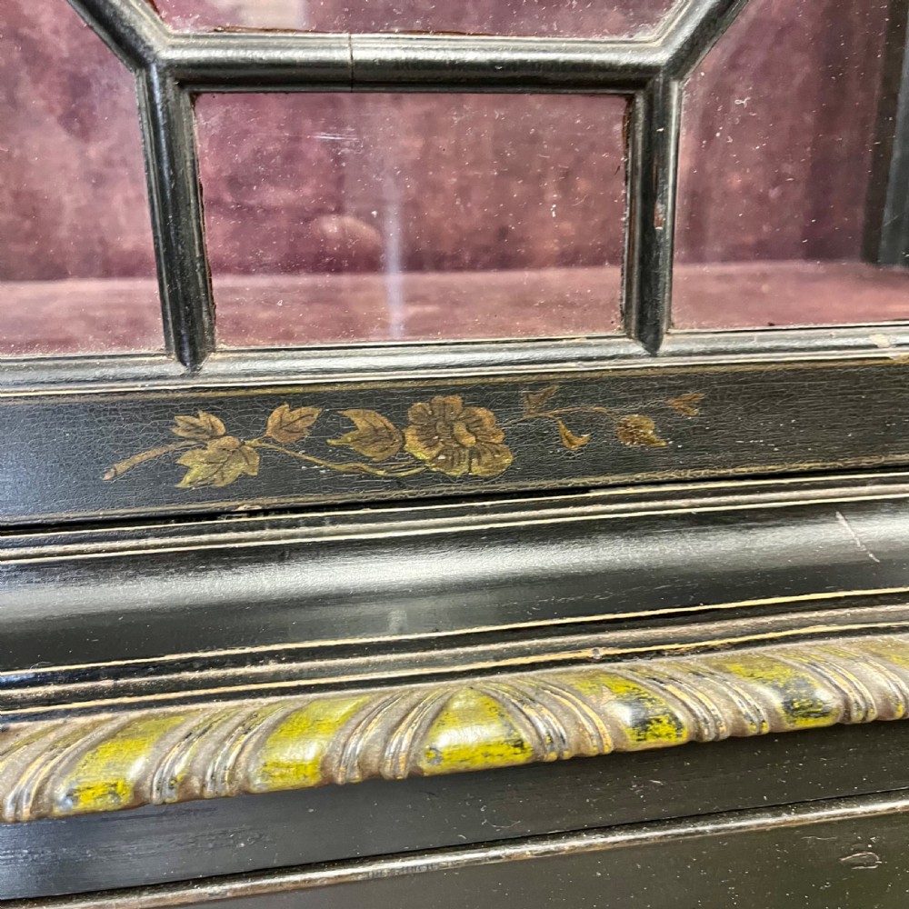 An ebonised Aesthetic Movement display cabinet featuring a glazed upper section with geometric glazing bars, hand-painted gilt motifs, a drawer, and slim legs with a bottom tier shelf. View XI