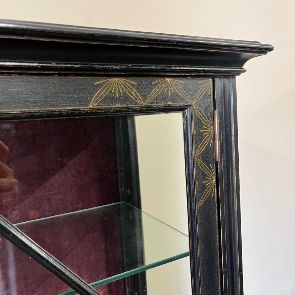 An ebonised Aesthetic Movement display cabinet featuring a glazed upper section with geometric glazing bars, hand-painted gilt motifs, a drawer, and slim legs with a bottom tier shelf. View XIII