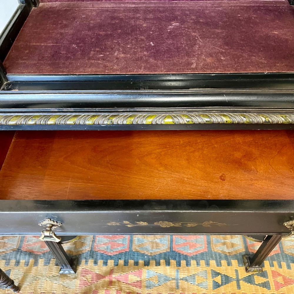 An ebonised Aesthetic Movement display cabinet featuring a glazed upper section with geometric glazing bars, hand-painted gilt motifs, a drawer, and slim legs with a bottom tier shelf. View XV