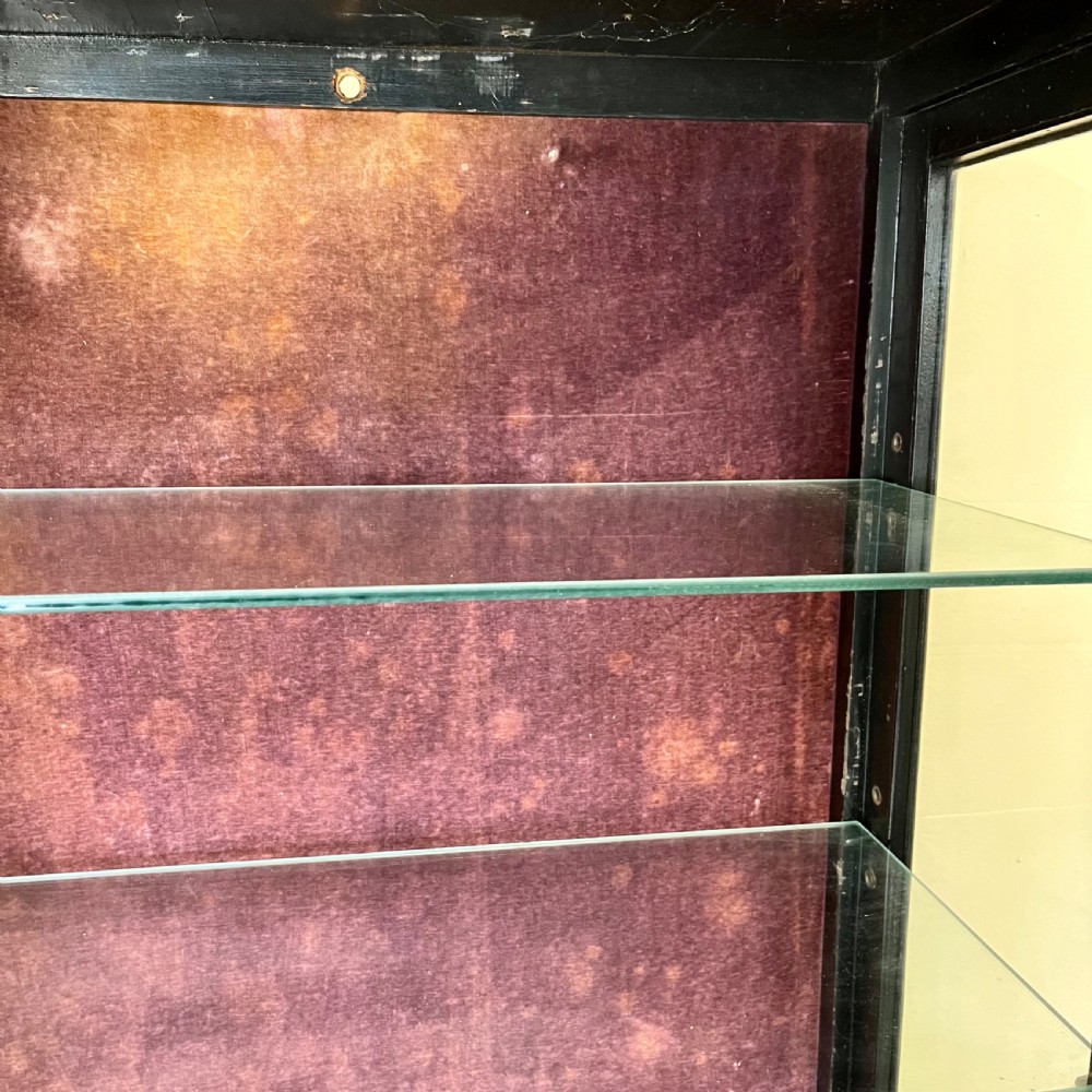 An ebonised Aesthetic Movement display cabinet featuring a glazed upper section with geometric glazing bars, hand-painted gilt motifs, a drawer, and slim legs with a bottom tier shelf. View XVI