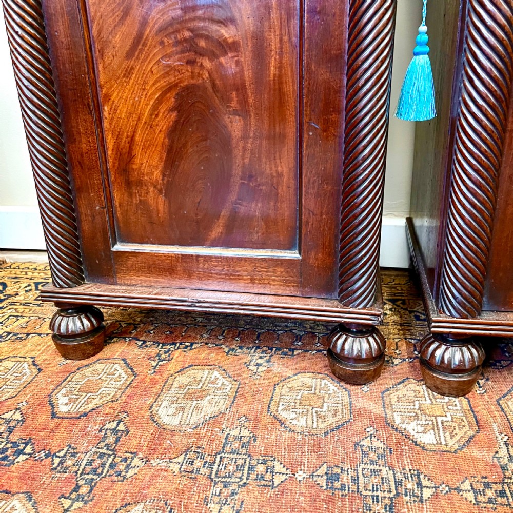 A pair of 19th-century mahogany bedside cupboards featuring flame mahogany panel doors, rope-twist carved side details, and turned feet. View V