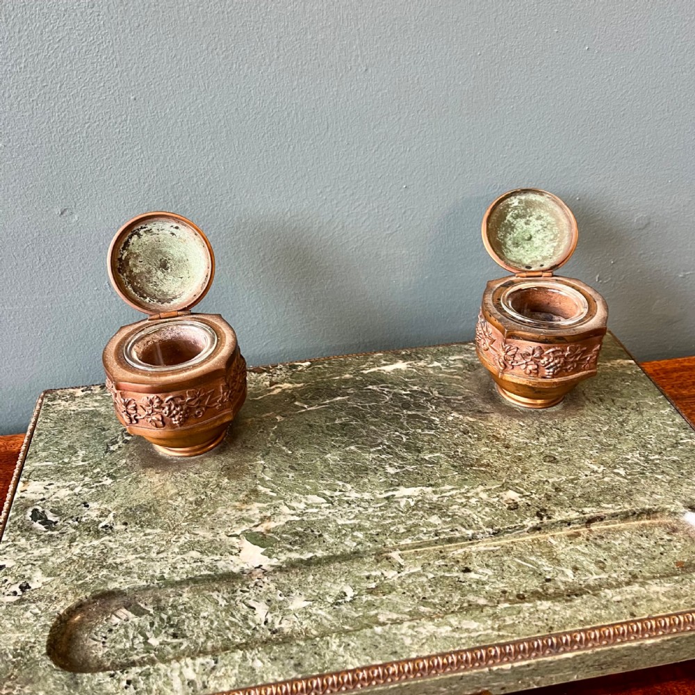 A French green marble desk set featuring a rectangular inkstand base with two raised gilt ormolu inkwells, a carved pen tray, ornate corner feet, and a matching marble rocking blotter. View V