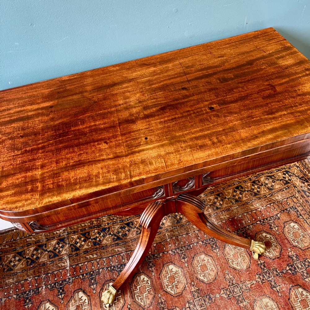 A 19th-century mahogany fold-over card table with a carved frieze, central pedestal, and splayed quadripartite legs ending in brass lion paw castors. View III