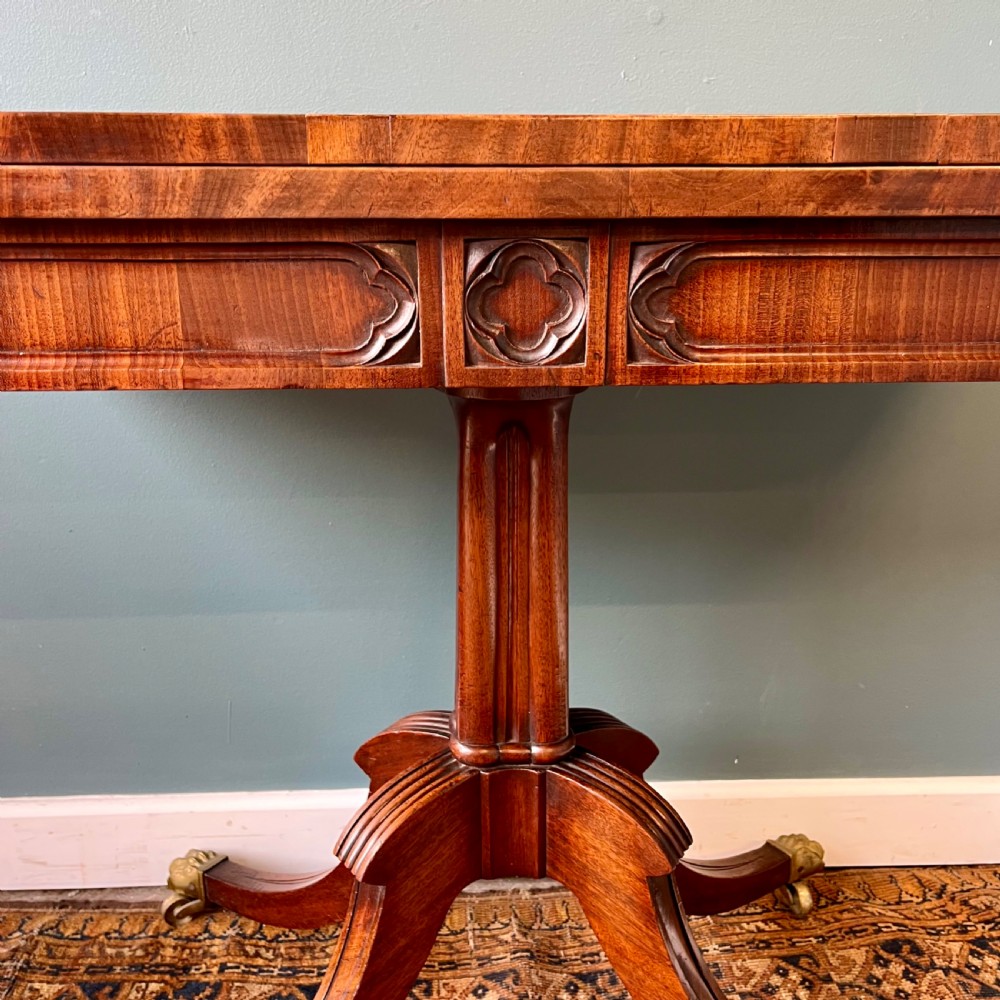 A 19th-century mahogany fold-over card table with a carved frieze, central pedestal, and splayed quadripartite legs ending in brass lion paw castors. View V