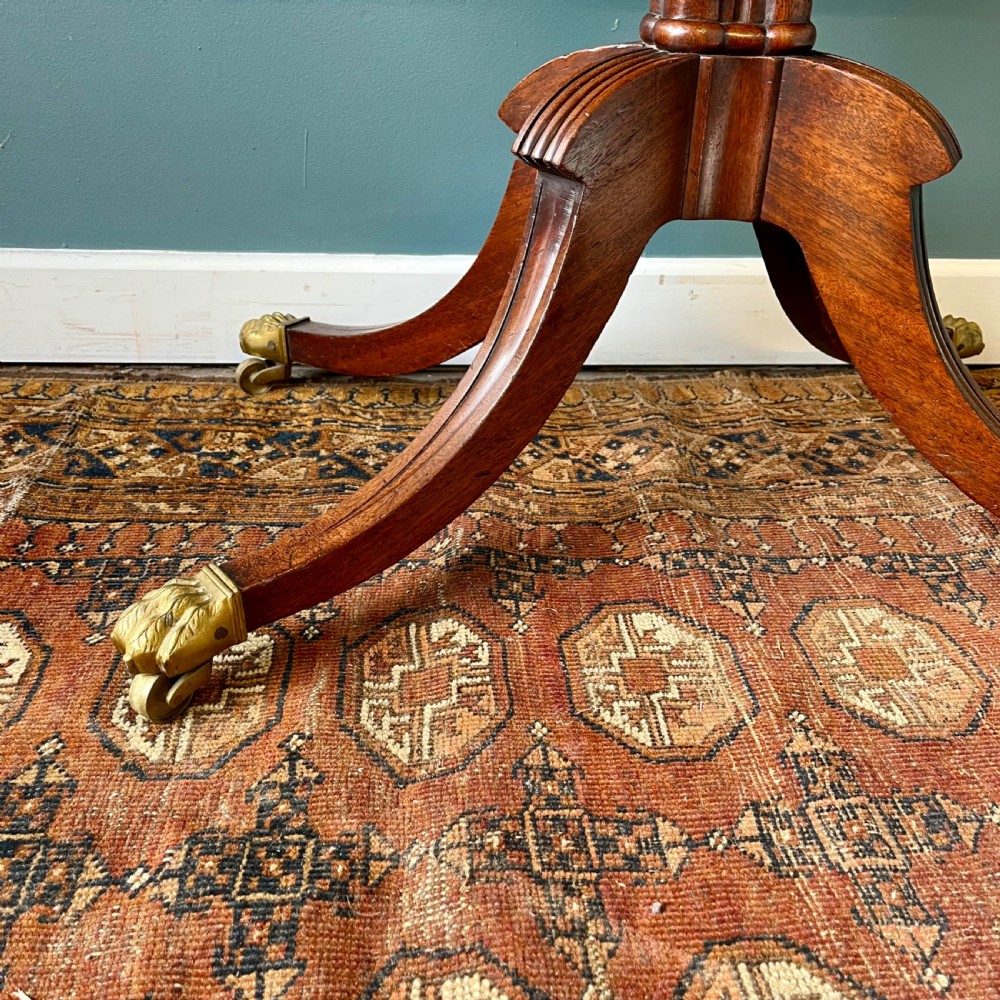 A 19th-century mahogany fold-over card table with a carved frieze, central pedestal, and splayed quadripartite legs ending in brass lion paw castors. View VI