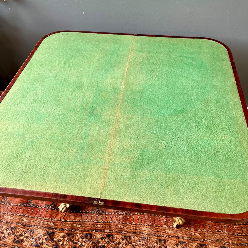 A 19th-century mahogany fold-over card table with a carved frieze, central pedestal, and splayed quadripartite legs ending in brass lion paw castors. View IX