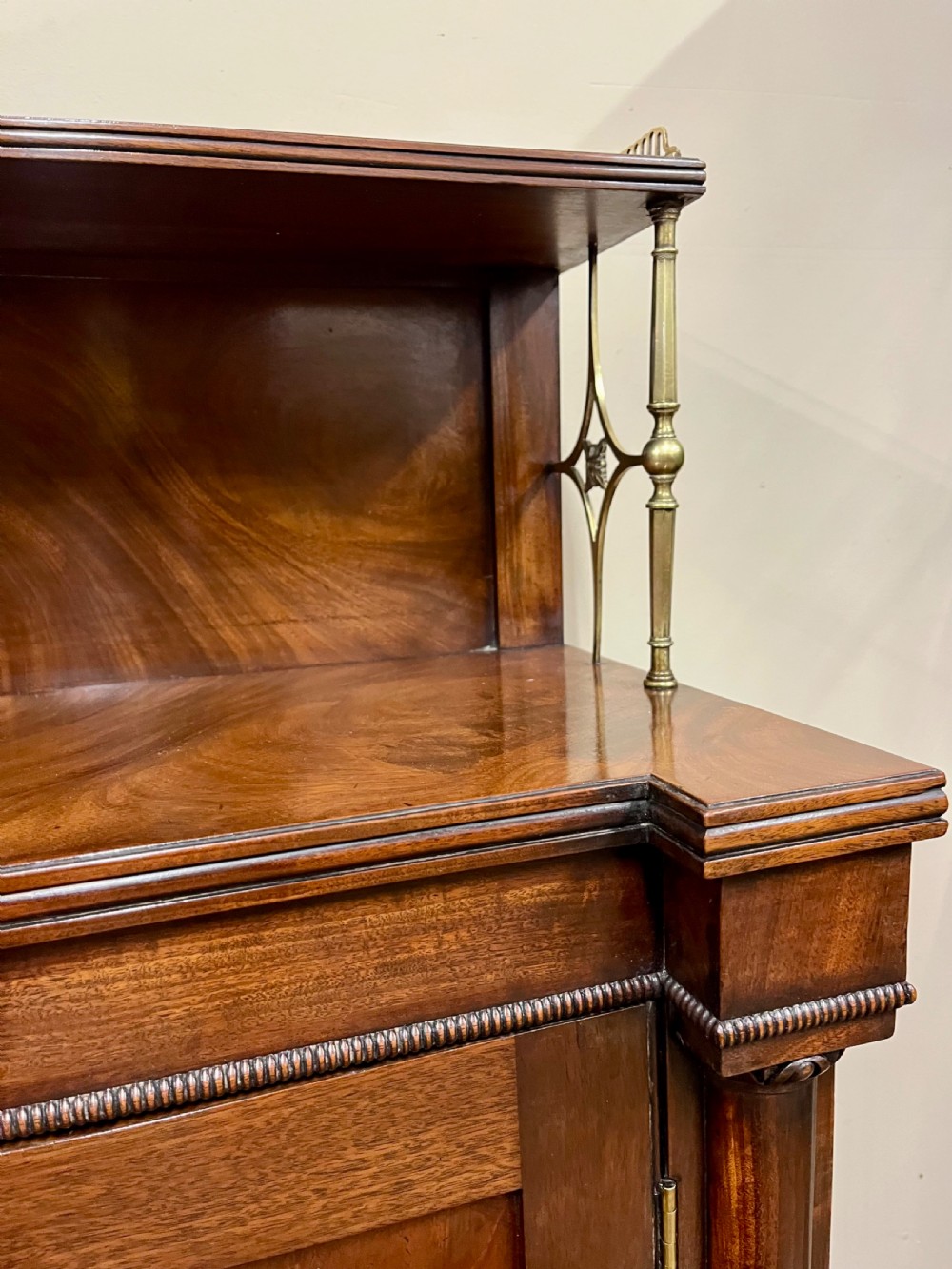 A 19th-century mahogany chiffonier featuring an upper shelf with a brass gallery, twin panelled cupboard doors flanked by turned side columns, resting on bun feet. View V