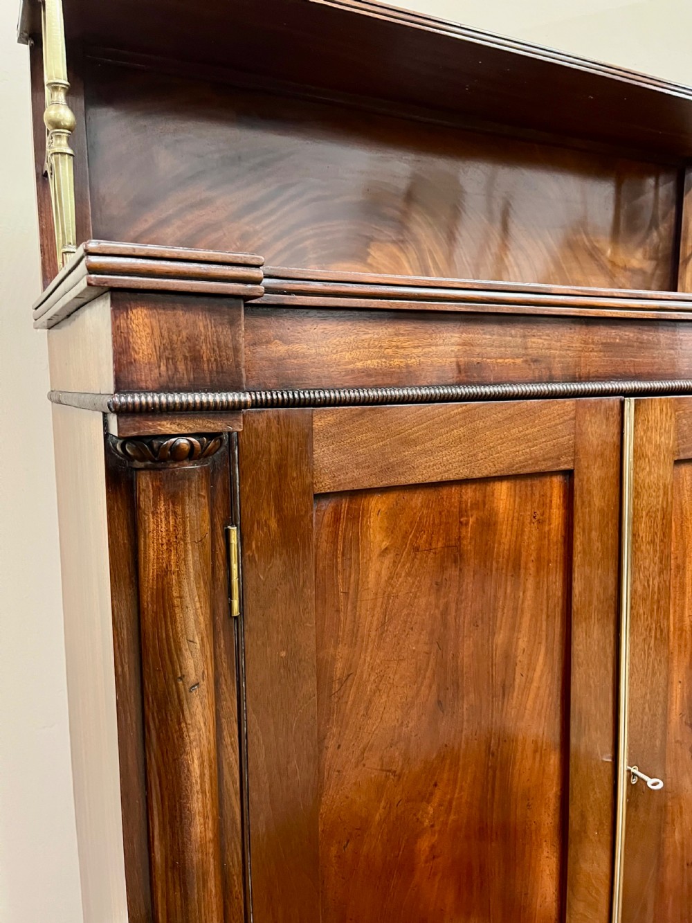 A 19th-century mahogany chiffonier featuring an upper shelf with a brass gallery, twin panelled cupboard doors flanked by turned side columns, resting on bun feet. View XI
