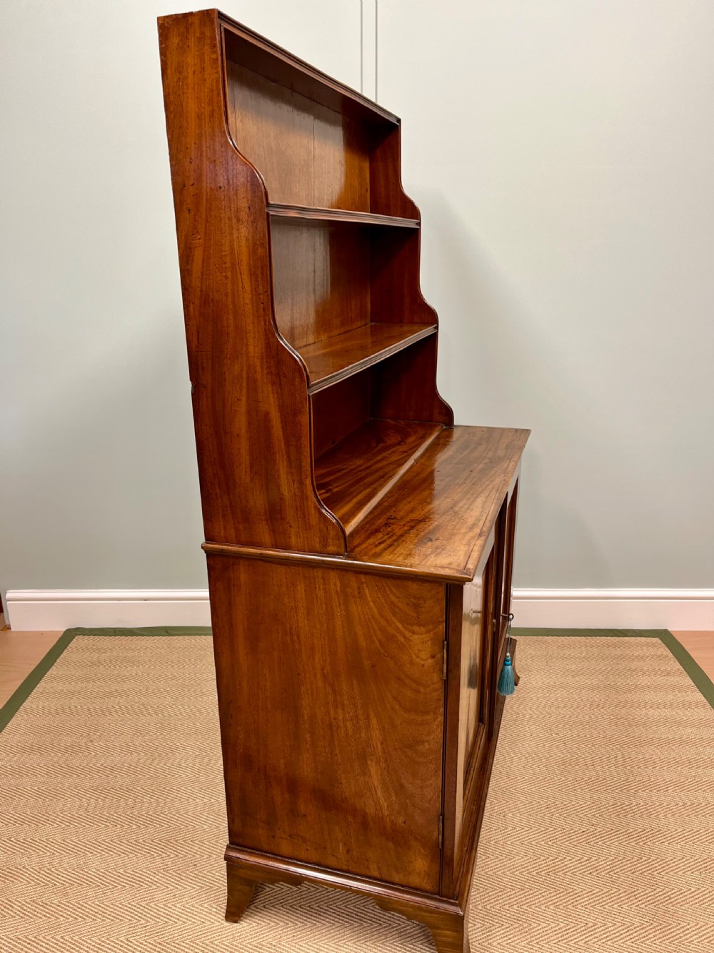 A 19th-century mahogany waterfall bookcase with three graduated open shelves over a two-door cabinet resting on bracket feet. View VI