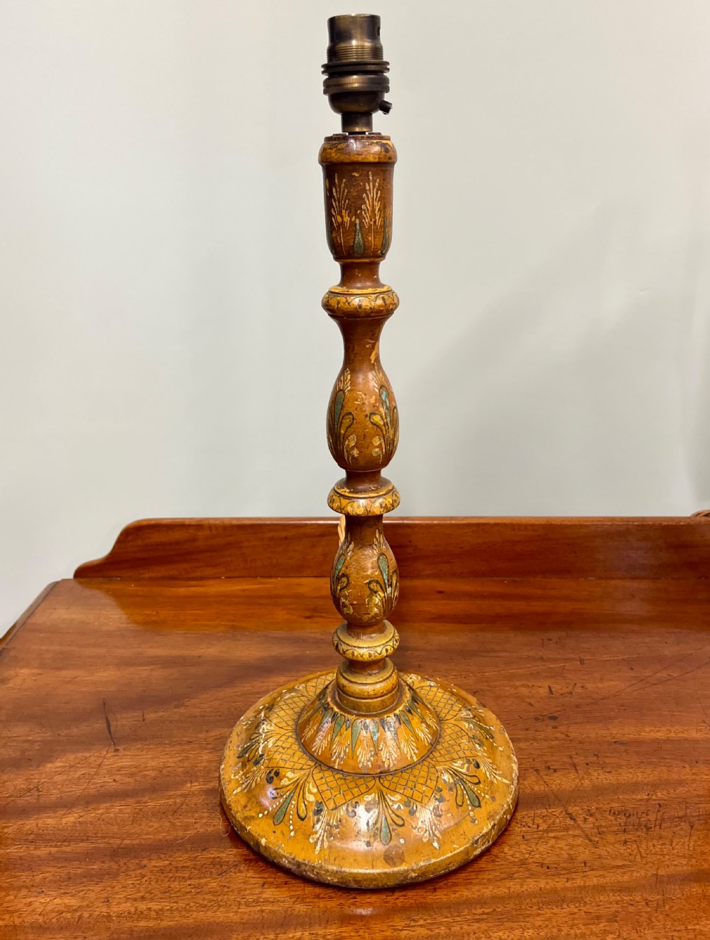 A 19th-century turned wooden Kashmiri table lamp base featuring hand-painted floral motifs in ochre, green, and white with a brass light fitting.