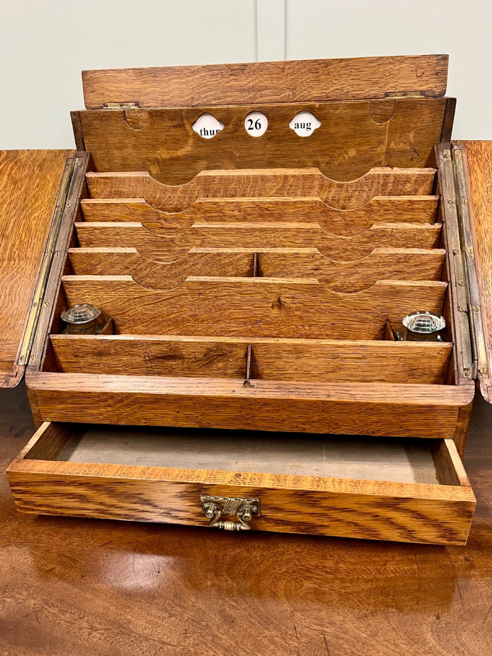 A Victorian oak stationery cabinet with open doors showing stepped letter compartments, a built-in calendar mechanism, inkwell slots, and a lower drawer. View X