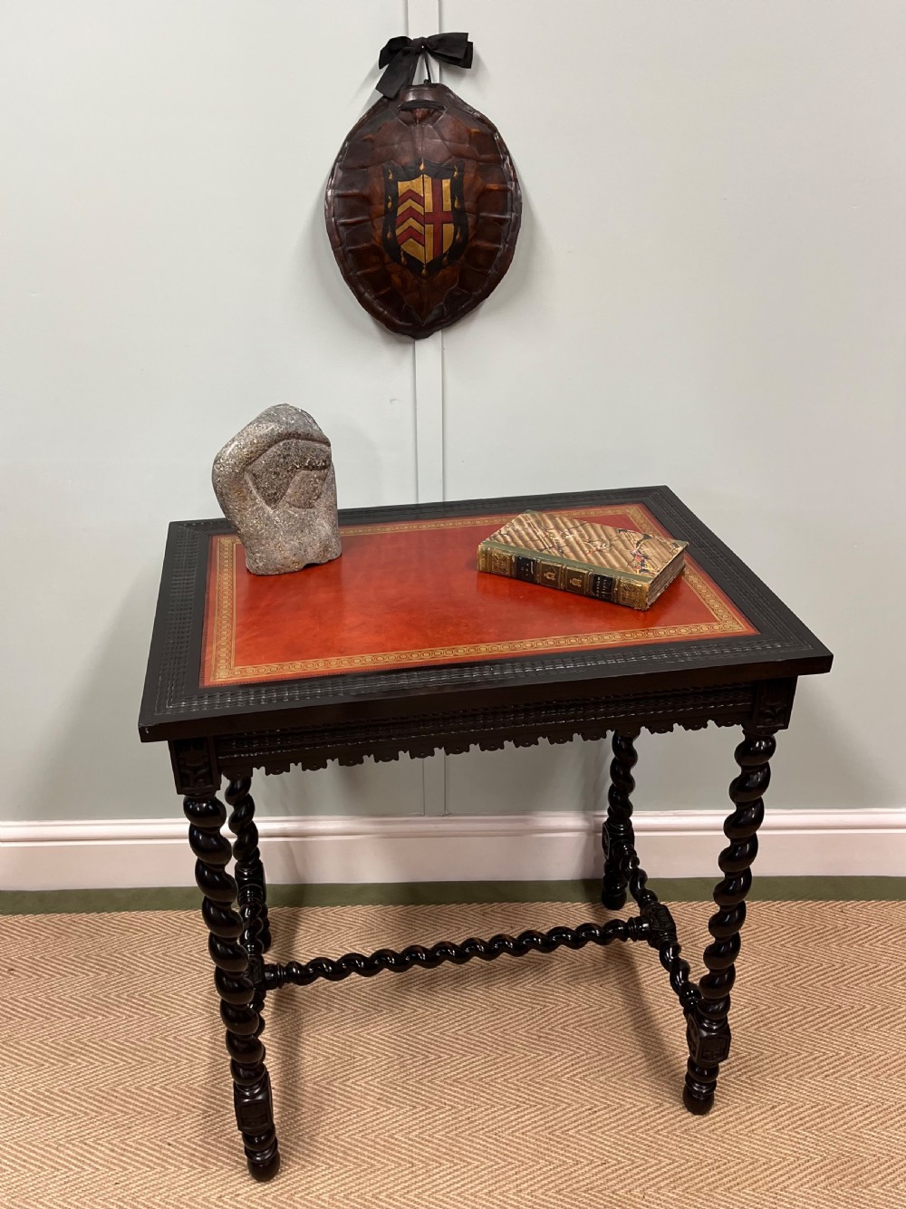 A 19th-century Spanish ebonised centre table featuring spiral barley twist legs, an under-stretcher, and an inset red leather top with gilded borders.