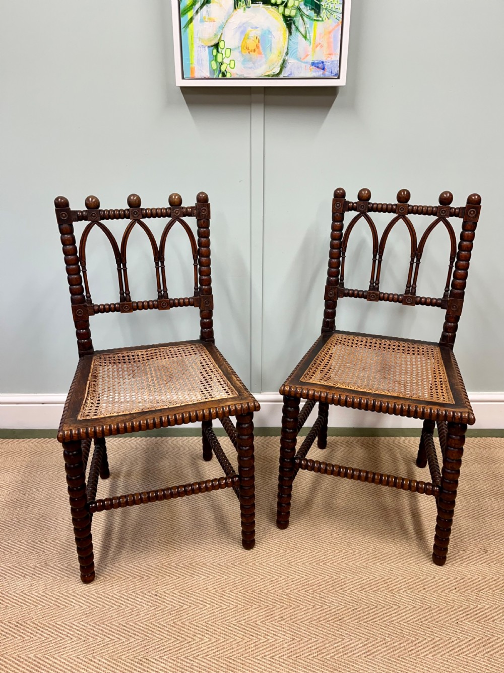 A pair of antique wooden chairs featuring intricate bobbin-turned framing and woven cane seats.