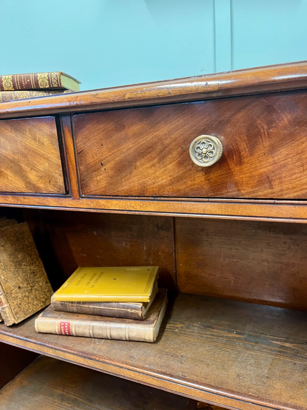 A low 19th-century mahogany bookcase featuring three small drawers above open shelving and supported by turned feet. View VIII