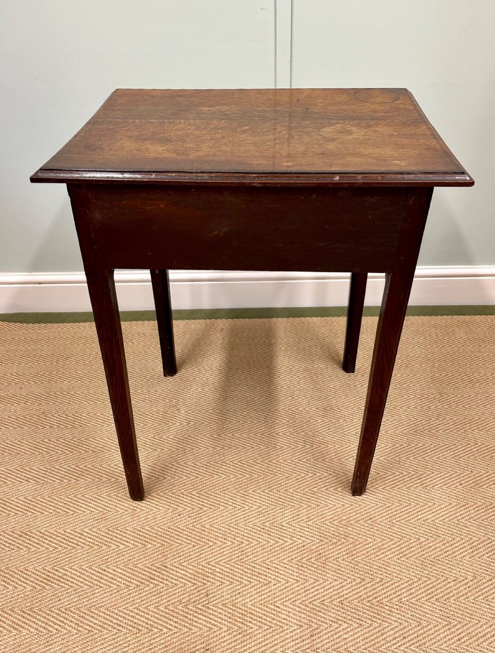 An 18th-century warm brown oak side table featuring a single drawer with a central brass handle and straight square legs. View X