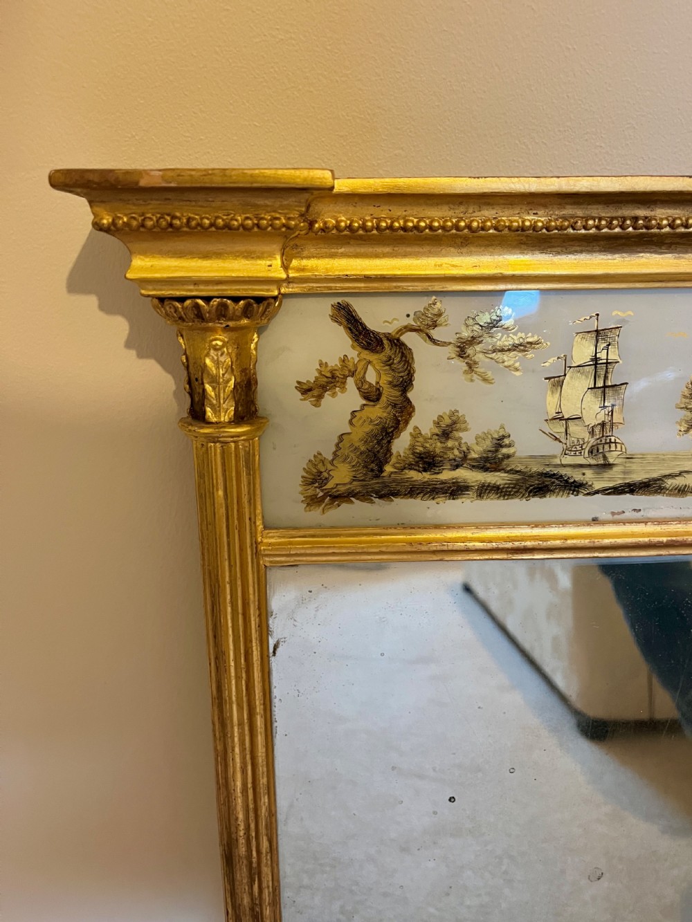 A tall Regency giltwood pier mirror featuring fluted side columns, an overhanging cornice, and a decorative top glass panel with a gilded landscape scene. View III