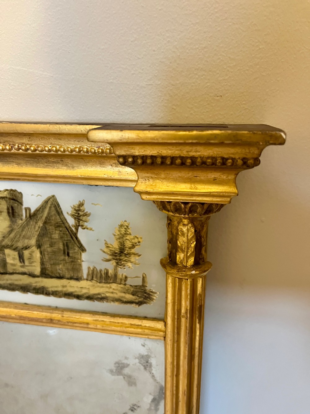 A tall Regency giltwood pier mirror featuring fluted side columns, an overhanging cornice, and a decorative top glass panel with a gilded landscape scene. View V