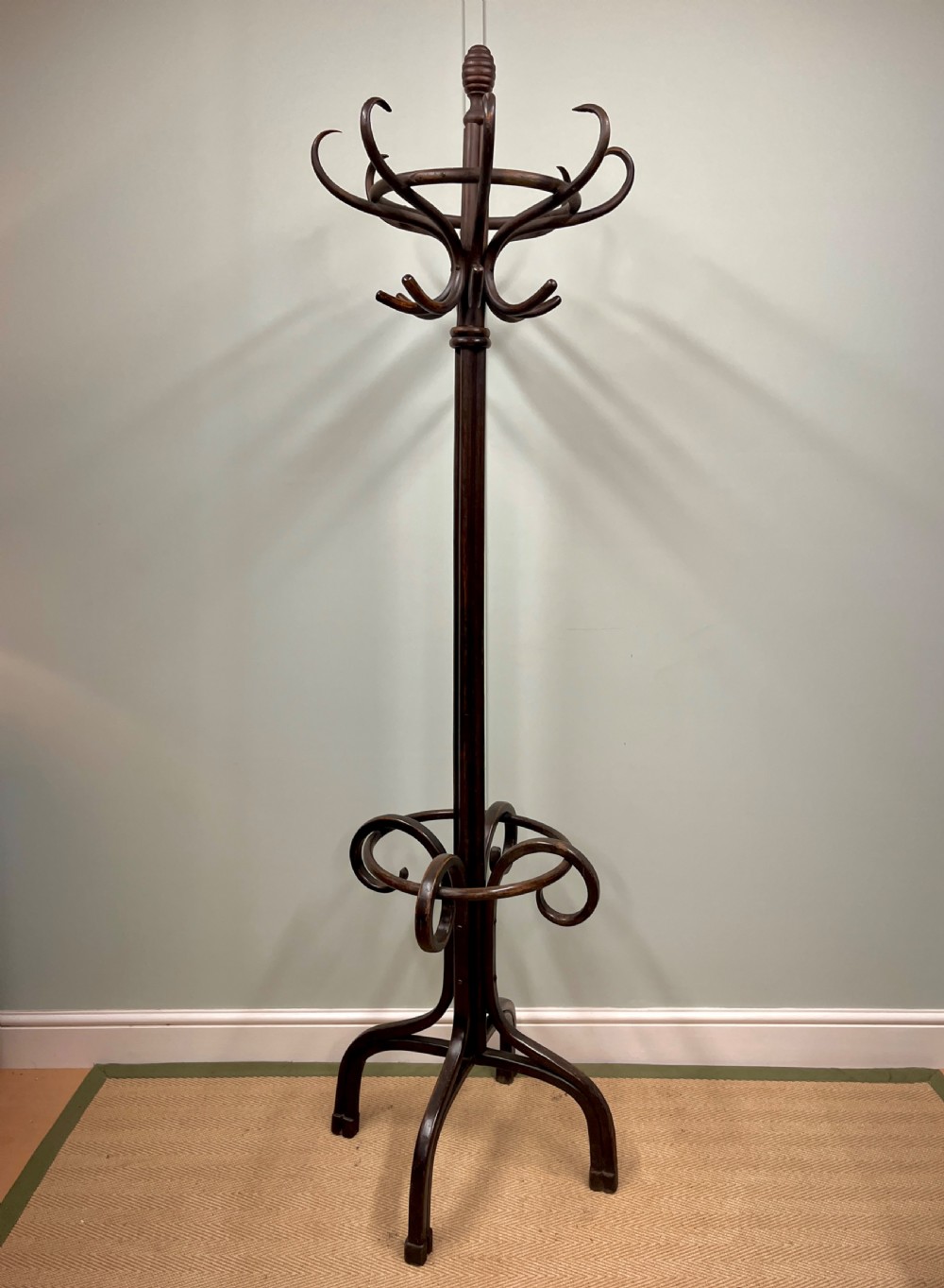 A dark brown Victorian bentwood coat and hat stand featuring curved upper hooks, a central turned column, an integrated umbrella ring, and quadrupled splayed feet.