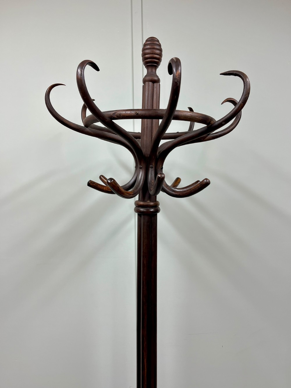 A dark brown Victorian bentwood coat and hat stand featuring curved upper hooks, a central turned column, an integrated umbrella ring, and quadrupled splayed feet. View II