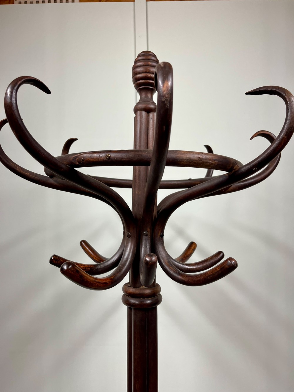 A dark brown Victorian bentwood coat and hat stand featuring curved upper hooks, a central turned column, an integrated umbrella ring, and quadrupled splayed feet. View VI