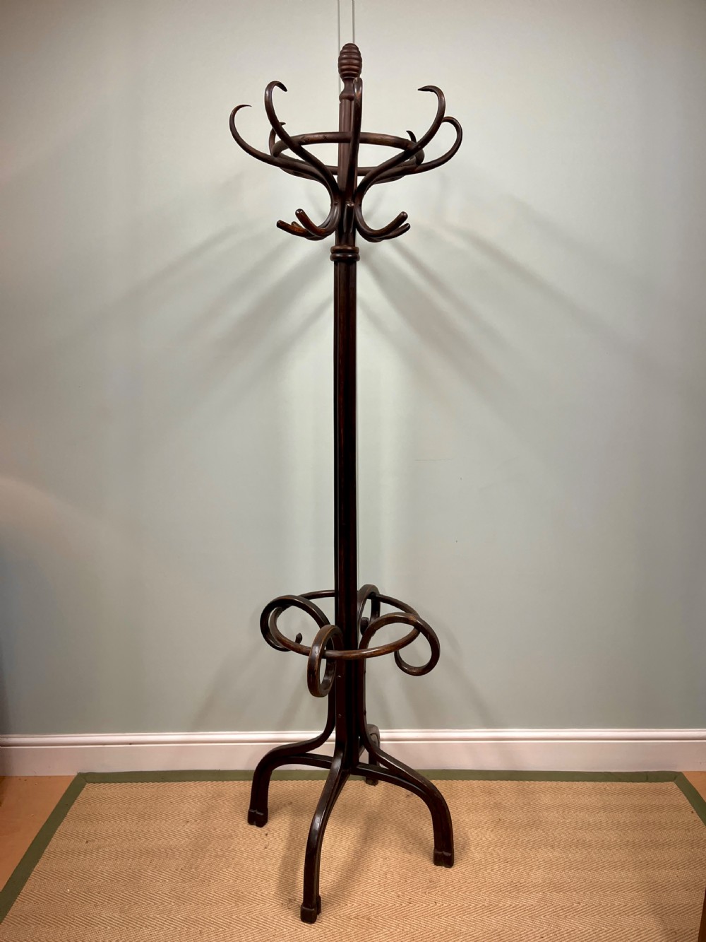 A dark brown Victorian bentwood coat and hat stand featuring curved upper hooks, a central turned column, an integrated umbrella ring, and quadrupled splayed feet. View VIII