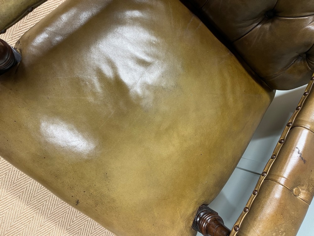 A 19th-century deep-buttoned tan leather armchair featuring padded armrests, brass studding, turned dark mahogany front legs, and castors. View VIII