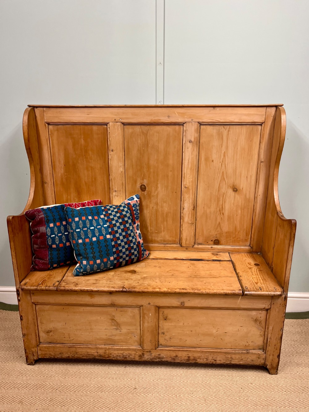 A 19th-century pine settle bench featuring a high panelled back, curved armrests, and an integrated hinged box storage base.