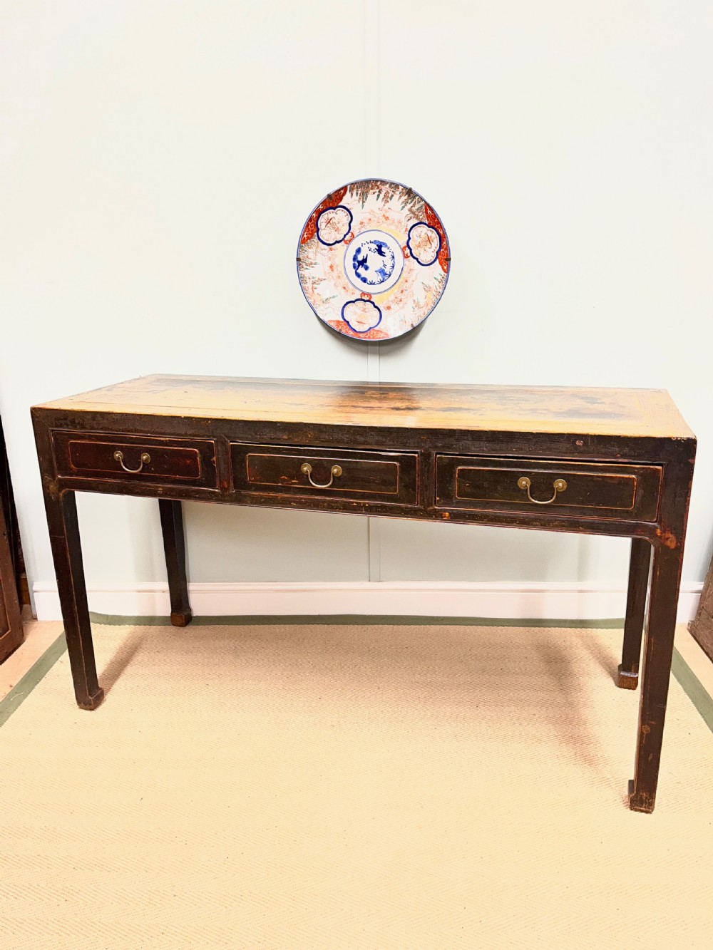 A 19th-century Chinese dark lacquered elm table featuring three drawers with brass drop handles and a long rectangular top.